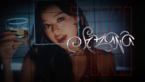 Suzana holding a drink in a dimly lit club scene from the official TIKI TIKI music video featuring VannDa.